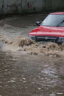 Um carro vermelho a passar no meio de uma estrada inundada